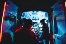 Paramedics stand around a patient in the ambulance, doors open.