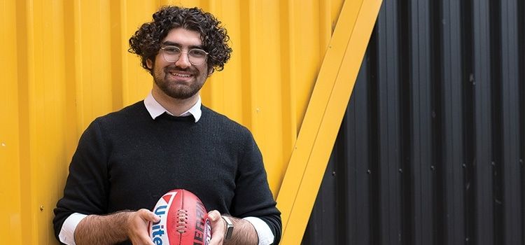 Osama – Swinburne student Swinburne design student,. Osama, holding a football outside Richmond Football Club as part of his internship experience.