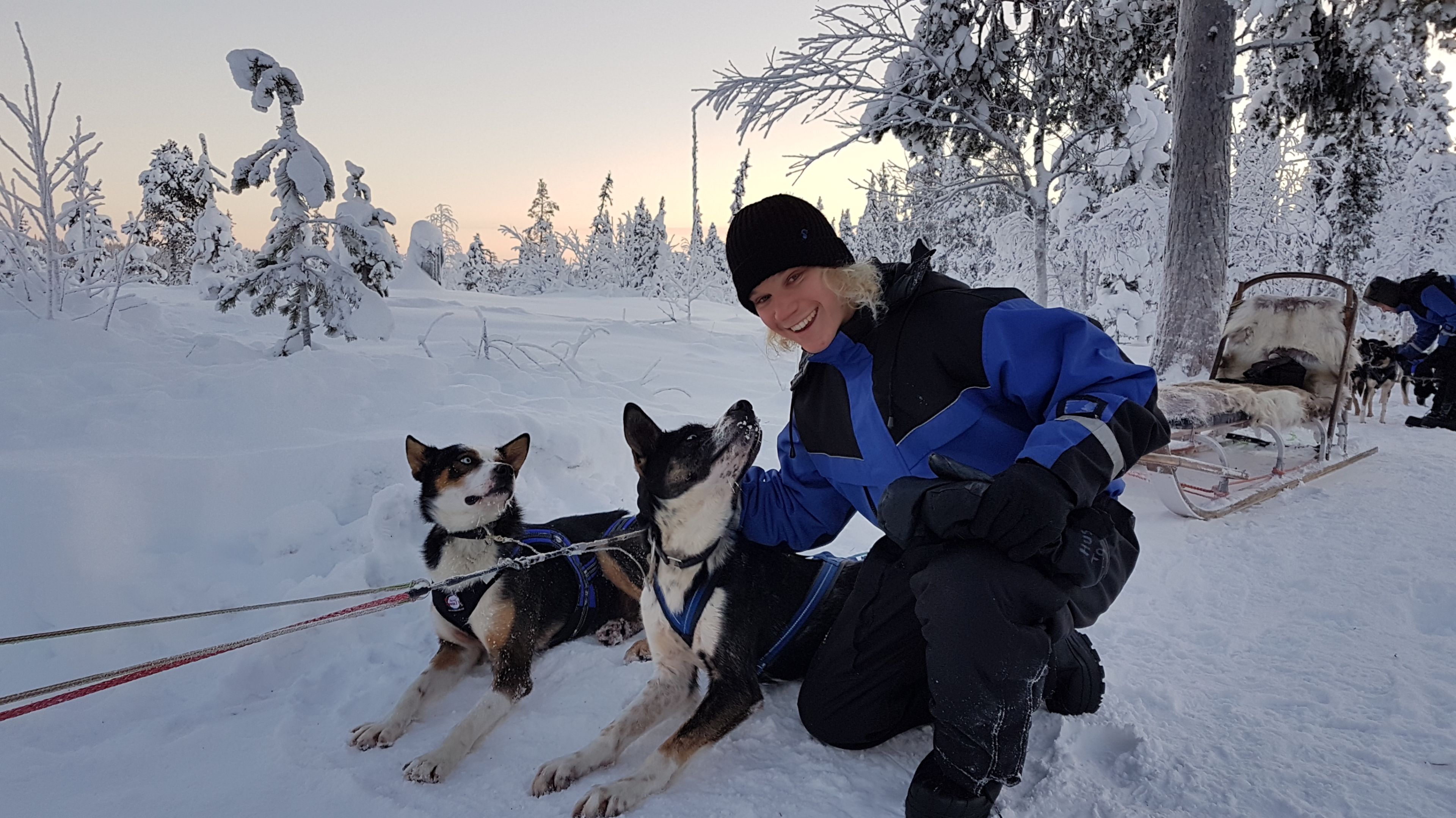 Study Abroad student, Sam, in Sweden Study Abroad student smiling a camera in snow covered Sweden with a dog sled in background